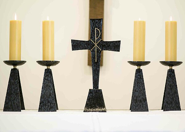 Bild: In der Mitte steht ein Kreuz und links und rechts stehen jeweils zwei gelbe Kerzen.