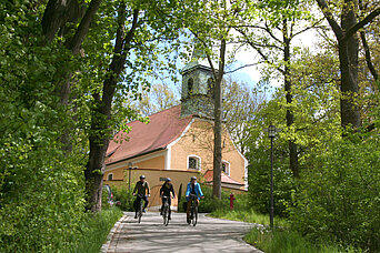 Bild: Fahrradfahrer, die einen Weg hinauffahren. Im Hintergrund ist die Kirche zu sehen.