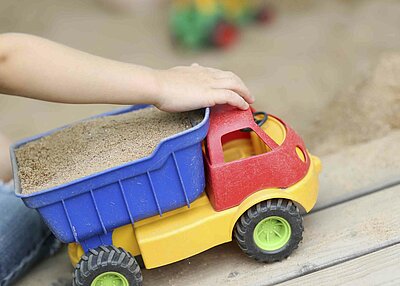 Ein Kind aus dem evangelischen Kindergarten Regenbogen, welches mit einem Spielzeuglaster mit Sand im Anhänger spielt. 