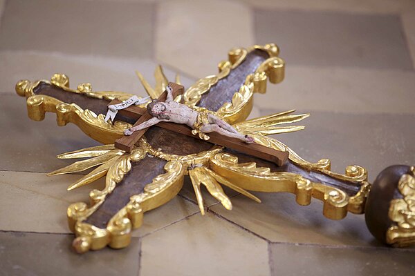 Bild: Ein braunes Jesuskreuz mit goldenem Rahmen.