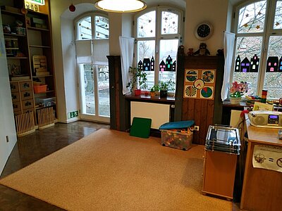 Gruppenraum mit Spielteppich und Fensterdekoration in der Kita An der Allee