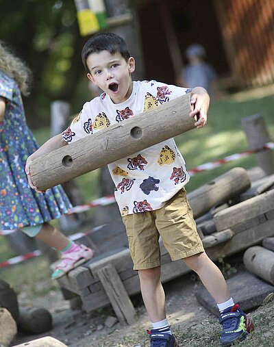 Ein Junge, der ein Stück Holz durch den Garten der St. Michael Kita in Weiden trägt.