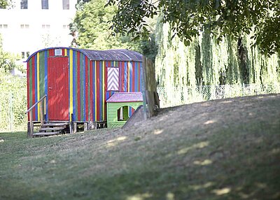 Ein in Regenbogenfarben bemalter Bauwagen, im Garten der St. Michael Kita in Weiden