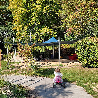 Kind fährt mit Rutschfahrzeug im Garten der Erlöserkita Amberg am Sandspielbereich vorbei