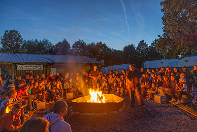 Viele Menschen, die beim Zeltlager 2022 in Plößberg um ein Feuer sitzen