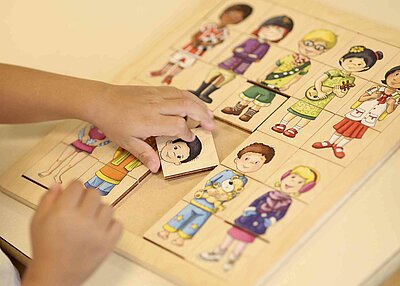 Ein Kind aus dem evangelisch lutherischen Kindergarten, welches ein Puzzelspiel macht, bei welchen man die verschiedenen Körperregionen den einzelnen Menschen zuordnen muss.