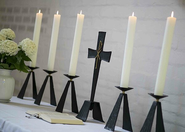 Bild: Ein Kreuz in der Mitte und links und rechts jeweils Kerzen.
