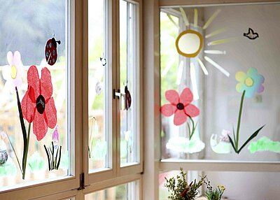 Kleine bunte Blumen, Marienkäfer und eine Sonne, welche an die Fenster des St. Markus Kindergarten in Weiden gemalt wurden.