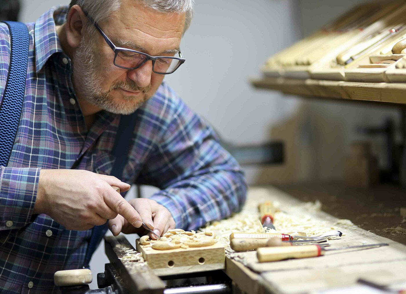 Bild: ein Mann, der in einer Werkstatt, ein Stück Holz zurechtschnitzt.