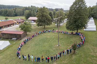 Eine Gruppe von Kindern beim Zeltlager des EJW, die in einem großen Kreis um ein Kreuz stehen.