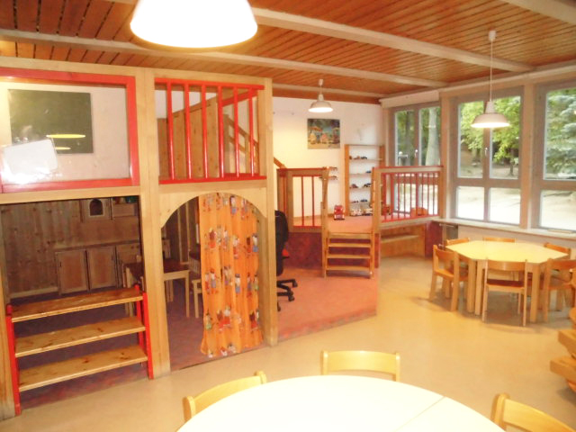Gruppenraum mit Holzspielhaus und Tischen in der Kita Loderhof